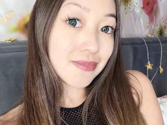 RenyLime with green eyes, brown hair, and pink lips, wearing a black mesh top, smiling at the camera. Her tits are not visible in this shot.