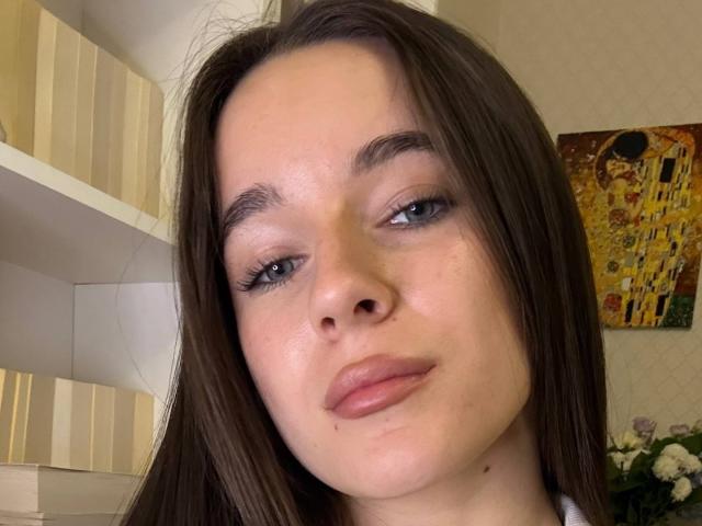 RobertWheler has fair skin, brown hair, blue eyes, and slightly parted pink lips. She's wearing eyeliner and has a small mole on her right cheek.