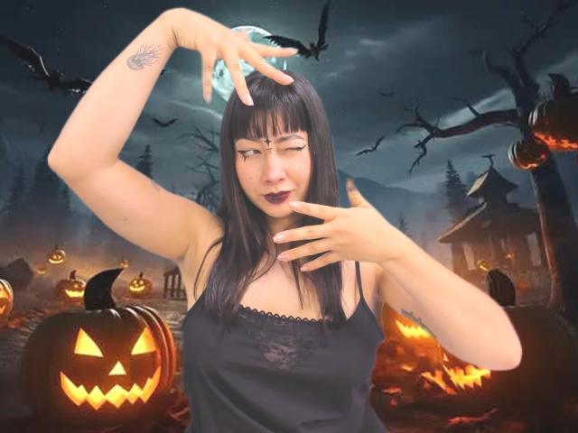 Genesiss with black hair, wearing a black lace camisole, winking, touching her head with one hand, surrounded by glowing jack-o'-lanterns, under a moonlit, spooky sky.