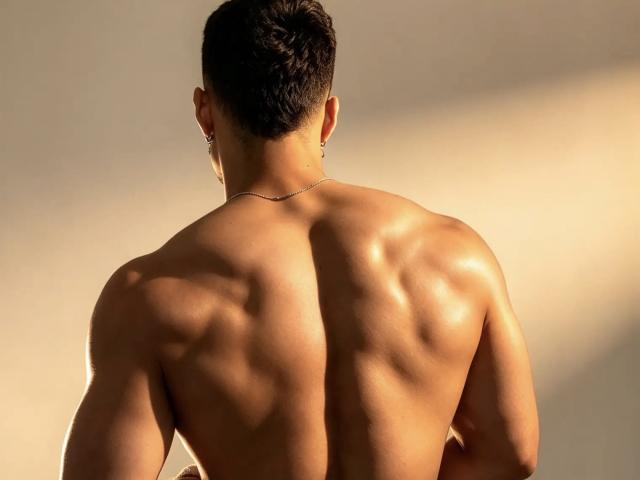 DominicSalazar's muscular back, shiny and glistening, shows defined muscles and a slim, sexy, toned ass. He has short, dark hair, small earrings, and a thin necklace.