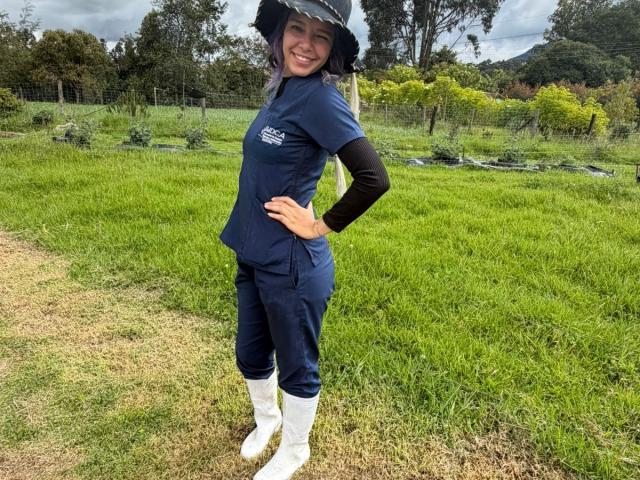 DarckVelvet with a smile, wearing a navy blue outfit, black long-sleeve shirt, white boots, and a black hat, standing in a grassy field. She's got a cute ass.