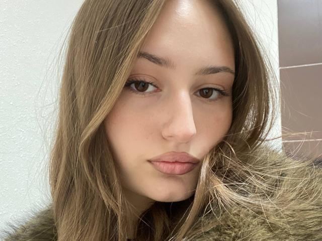 TiffanieLongton has light brown hair, brown eyes, and pink lips, wearing a fur-lined jacket, with a neutral facial expression, looking slightly to the right in a selfie.