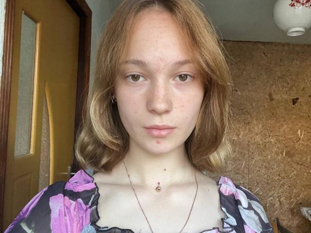 Loni Tockey tem cabelos castanho-claros, que chegam aos ombros, olhos verdes e uma pequena marca de beleza abaixo do queixo. Ela está vestindo uma blusa florida e um colar fino..