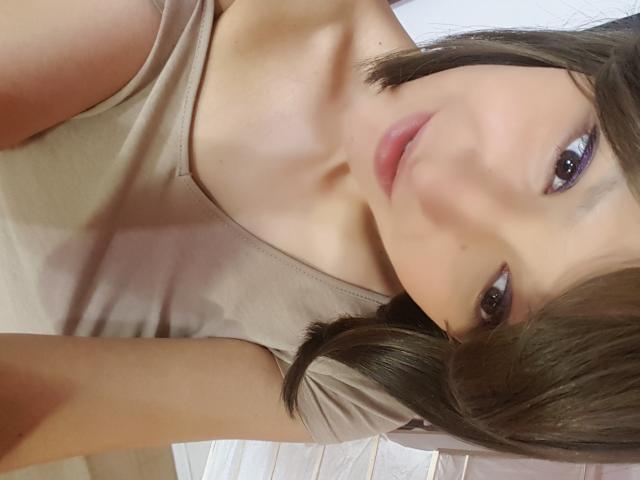 AmethystCharm has brown eyes, a cute face, and pink lips. She's wearing a beige top, with her brown hair partially covering her right eye. Her tits are visible.