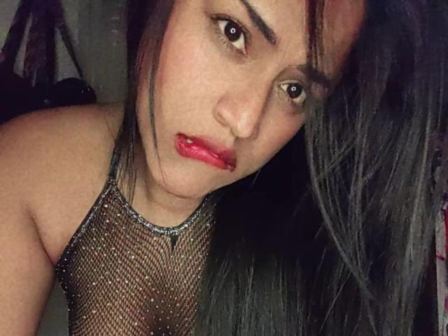 IvannaDuran69 with red lipstick, black mesh top, and long dark hair, looking seductively at the camera, her pouty lips and dark eyes adding to her sexy appeal.