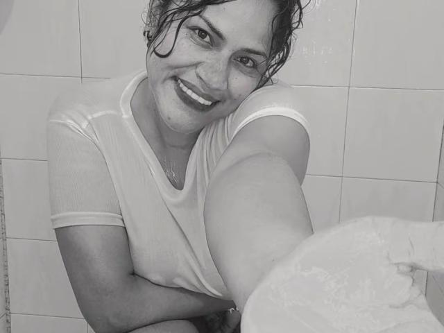 IvannaDuran69 with wet, see-through shirt, smiling, sitting in a shower, one leg up, holding a soap suds, curly dark hair, medium skin, small breasts, cute, happy.