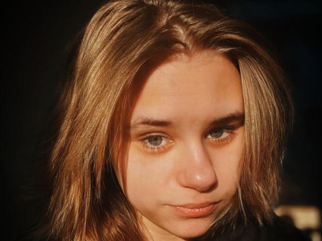 IngerKennington has light brown, shoulder-length hair, blue eyes, and a slightly serious expression with sunlit highlights in her hair. Her nose is small, and her lips are slightly pursed.
