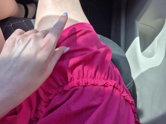 Rozalin's pink skirt, hand with purple nail polish pointing at her bare, light-skinned belly, car seat in background. Her skirt's waistband is slightly raised.