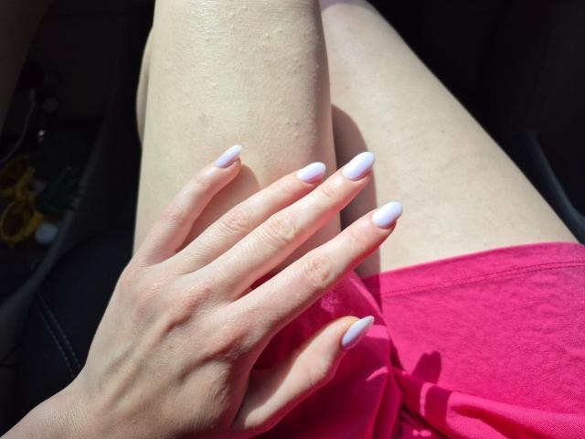 Rozalin's hand with pale pink nails rests on her bare thigh, wearing a pink skirt, sunlight highlighting her skin and fingers. Her leg is slightly bent, showing a shadow.