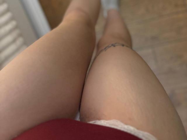FallenAngelia's thighs are in the frame, showing smooth, fair skin with a small tattoo on the right thigh, and she's wearing white lace and red clothing.