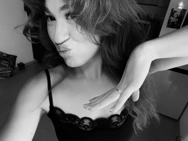 Black-and-white selfie of SerenaHuseth with long wavy hair, pouty lips, and a cute smile. She's wearing a lacy black top, hand on chest, showing a ring.