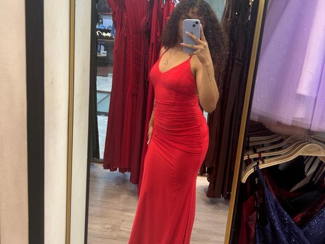 Sofia, leidenschaftlich in einem engen roten Kleid, das ihr Gesäß und ihre Brüste zeigt, hält ein Handy in einem Spiegel-Selfie, mit lockigen Haaren und einer selbstbewussten Pose..