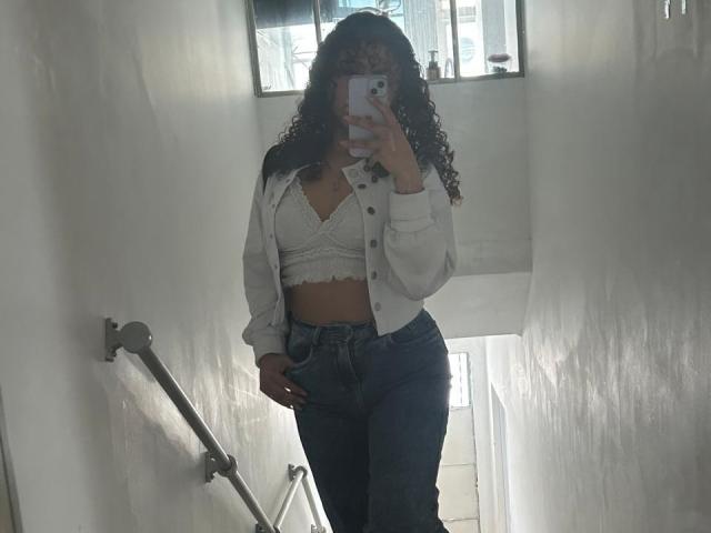 SofiaPassionne with curly hair, wearing a white lace bralette, open white shirt, and high-waisted blue jeans, taking a mirror selfie, showing her tits and ass.