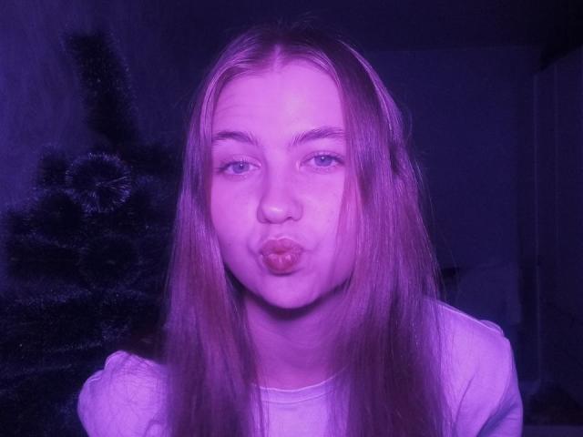 MargretWarriner with long pinkish-purple hair, puffy lips making a kissy face, blue eyes, wearing a white shirt, in a purple-tinted photo. Her ass is not visible.