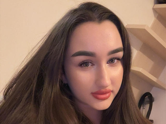 FortuneLisa69 with long brown hair, thick eyebrows, full red lips, and brown eyes, looking directly at the camera with a slight smile. Her skin is smooth and fair.