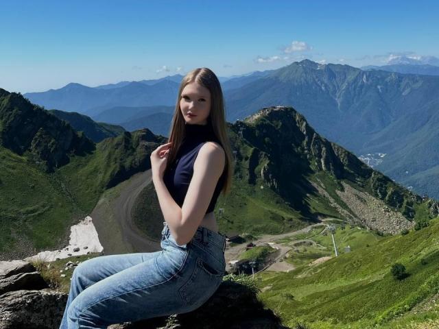 Solange Gulsvig, avec ses longs cheveux blonds, ses petites seins, vêtue d'un haut noir sans manches et d'un jean bleu, est assise sur un rocher dans un paysage de montagne, les mains près de son visage..
