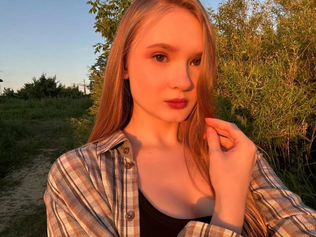 Solange Gulsvig, avec de longs cheveux blonds, portant une chemise à carreaux déboutonnée, un haut noir et du rouge à lèvres, touchant ses cheveux, baignée par la lumière chaude du coucher de soleil. Ses seins sont légèrement visibles..
