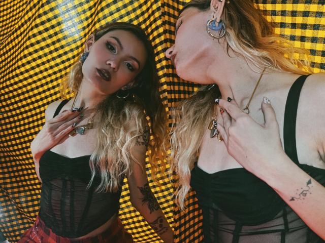 AlanisBlanc, avec ses cheveux blonds ondulés, son haut en maille noire, ses boucles d'oreilles et ses tatouages, regarde son reflet. Elle touche son cou et a une expression sexy et confiante..