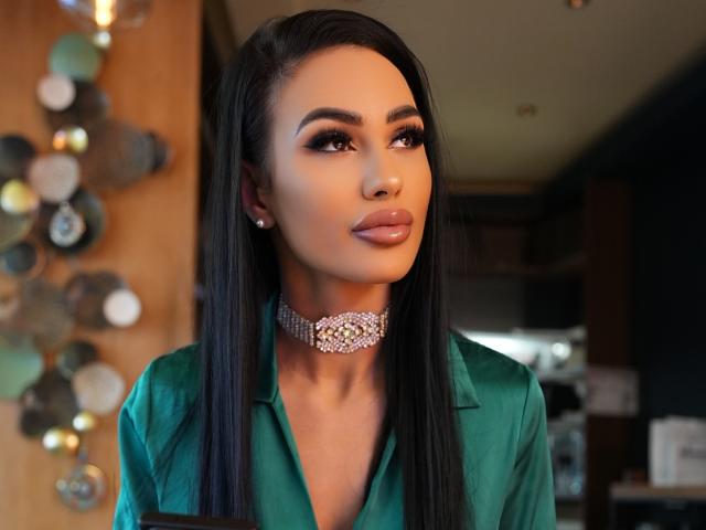 CharlotteAria with long black hair, green shirt, and sparkly choker, looking up with glossy lips, full eyebrows, and subtle makeup. Boobless, focused, and elegant.