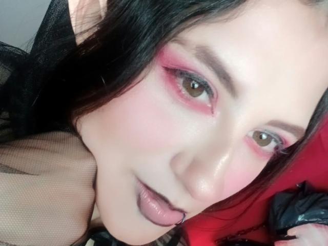 MaryCruzz with pink eyeshadow, black lipstick, and tongue piercing, showing off her sexy face with long black hair and a slight smile, in a provocative selfie.