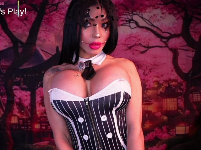 SandraXSeins with huge tits in a pinstriped corset, black bowtie, ball gag, and black wig. She's wearing makeup with pink lipstick, and has tattoos on her shoulder.