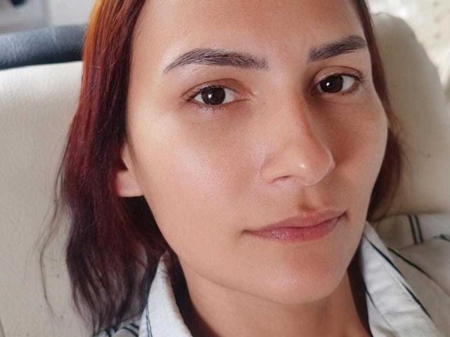 RenataNoir's face, with brown eyes, light skin, and reddish-brown hair, showing a slight smile and natural makeup. Her eyebrows are thick, and she's wearing a striped shirt.