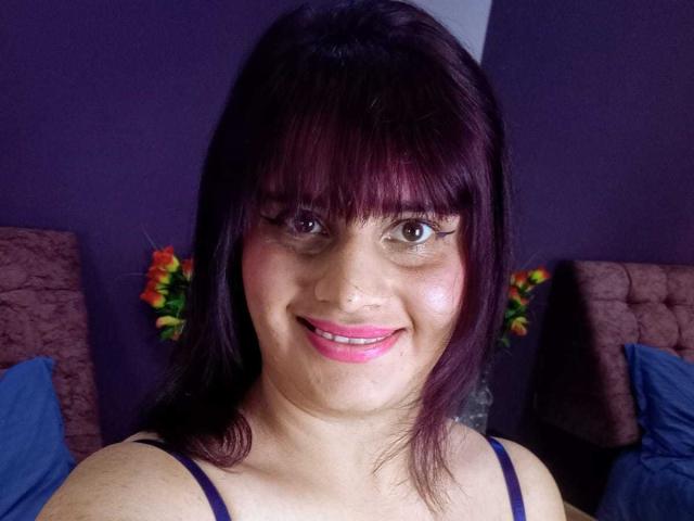 VivianFranco with dark purple hair, bangs, and pink lipstick, smiling, wearing a black spaghetti strap top, showing her nose ring and pinkish skin. Her tits are small.