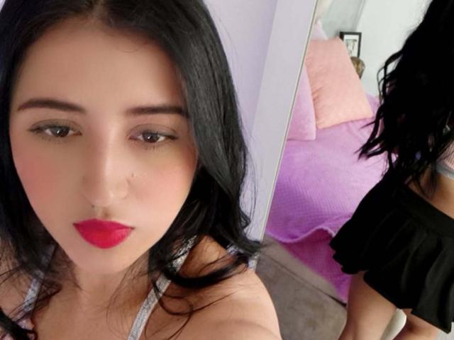 NicollJeans with black hair, red lipstick, and a nose ring, wearing a black top, showing her back in a mirror selfie, with visible tits.
