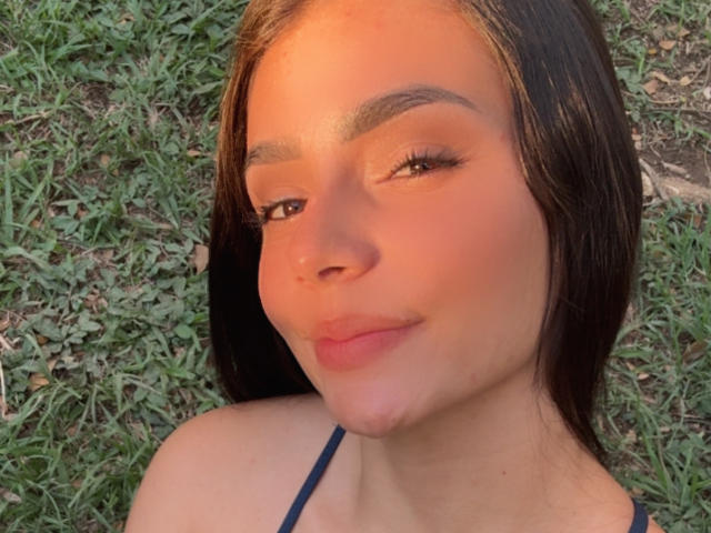 KimmyK has smooth brown skin, long dark hair, and is smiling with slightly pouty lips. She's wearing a blue strap top and has well-defined eyebrows.