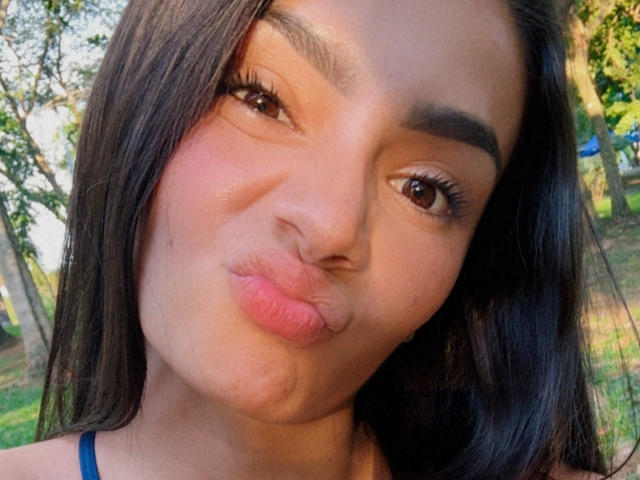 KimmyK's face with pouty, puckered lips, brown eyes, long black hair, and thick eyebrows, wearing a blue top, showing a cute, playful expression.