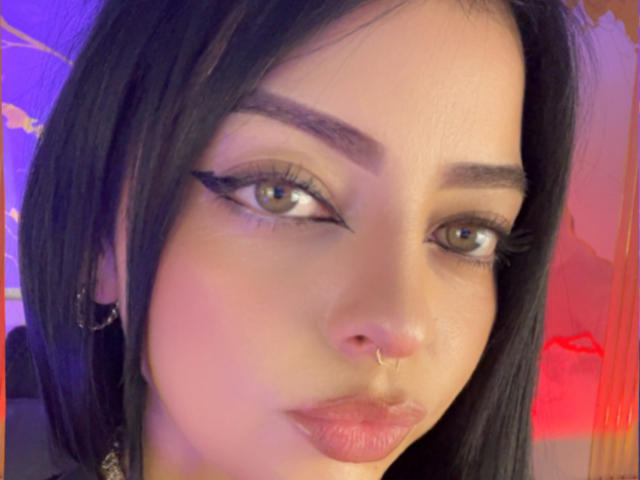 LilithAmoth a les cheveux noirs, un anneau au nez et un trait d'eye-liner ailé. Ses yeux verts sont légèrement en amande, et elle a les lèvres roses et brillantes. Ses sourcils sont épais et bien dessinés..