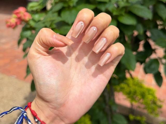 IsabellaJames's hand with long, nude-painted nails, slightly curved, showing off her glossy, glossy tips. She's wearing a colorful bead bracelet.