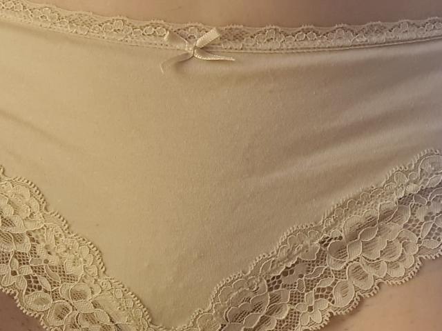Anne Ross' cremefarbene Spitzenunterwäsche mit zarten Spitzenkanten und einer kleinen Satinschleife am oberen Rand, die eine weiche, detailreiche Ansicht ihrer Vulva zeigt..