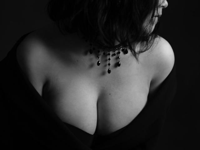 Simerria's big tits are exposed in a black and white shot, wearing a dark choker with bead drops, and a loose black top falling off her shoulders.