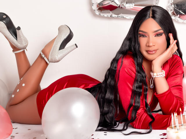 NatLewis lying on her stomach, wearing a red dress, silver heels, long black hair, and a bracelet, with her ass up and a white balloon in front.