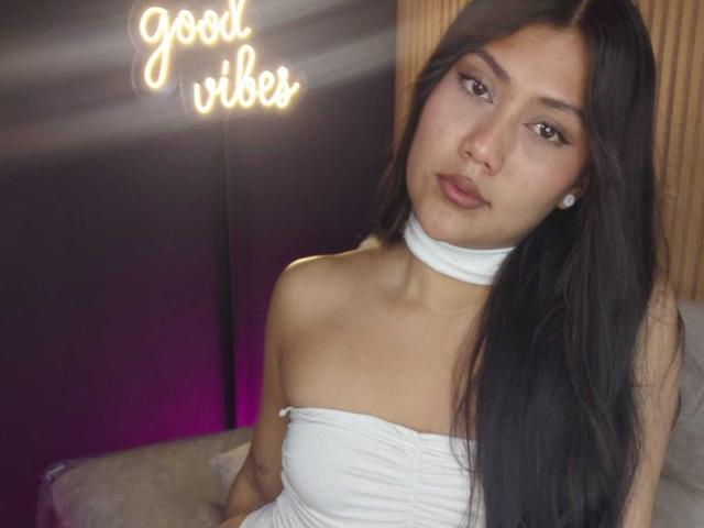 Catalehia69 with long black hair, wearing a white strapless top, has a cute face, small earrings, and a white choker. Her tits are barely visible. Soft light.