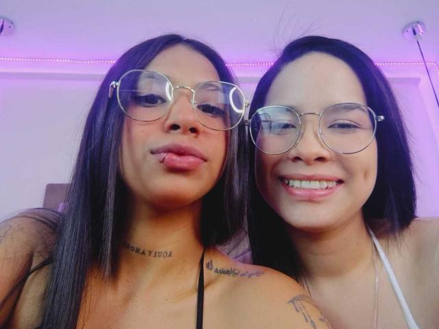 DakotaandJuliette with long black hair, wearing glasses, sticking out tongue, tattoos on neck and shoulder, smiling next to DakotaandJuliette with similar hair, glasses, and white halter top.