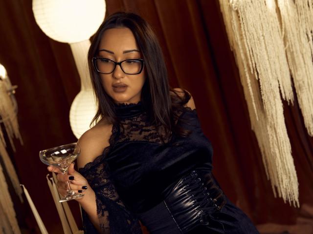 EvaSarazardje with black lace dress, glasses, and corset, holding a martini glass, brown hair, looking seductive, dark nails, medium tits, in a dimly lit, elegant room.