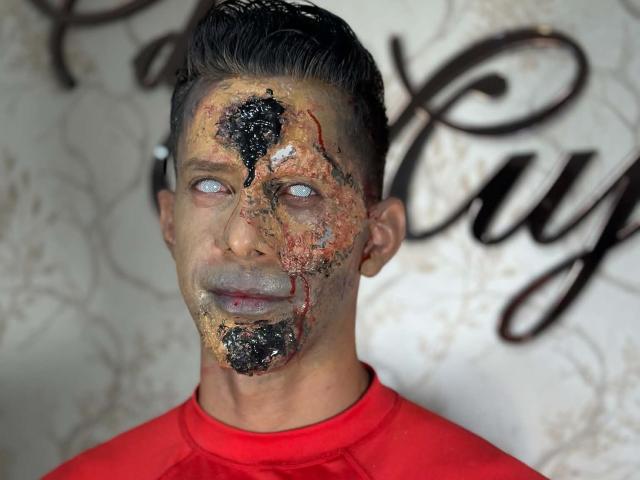 JoseRumBerotop tem um rosto sujo e coberto de lama, com manchas pretas e vermelhas, olhos azul-claros e cabelo curto e escuro, vestindo uma camisa vermelha, com uma expressão intensa e suja..