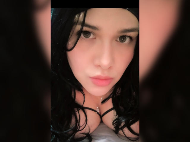 VivianaThompson has black curly hair, pale skin, and full pink lips. She's looking at the camera with large brown eyes, showing her cleavage with black straps.