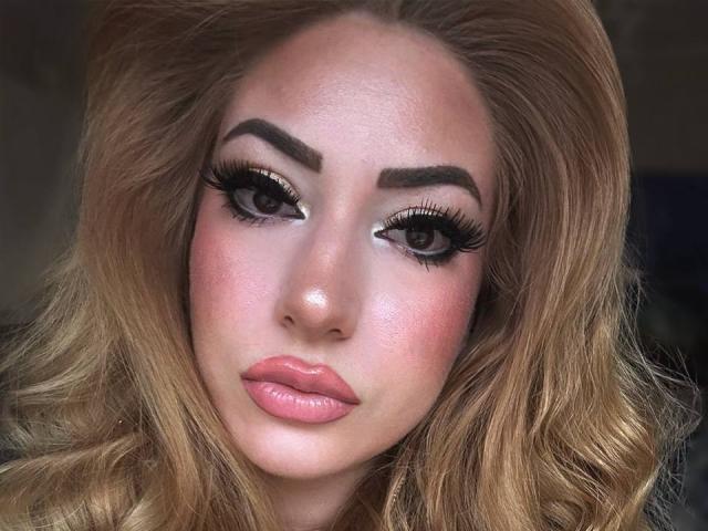 ElviraCrichlow has shiny blonde hair, thick eyebrows, long black eyelashes, pink glossy lips, and a slightly flushed face. Her brown eyes look directly at the camera.