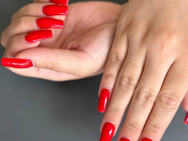 GeraNia's hands with shiny red, long, square-tipped nails, showing off her perfectly manicured fingers against a gray background. Her nails are glossy and super cute.