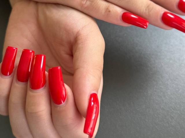 GeraNia's hand with shiny red nail polish on long, glossy nails, fingers slightly curled, showing off the bright, vibrant color.