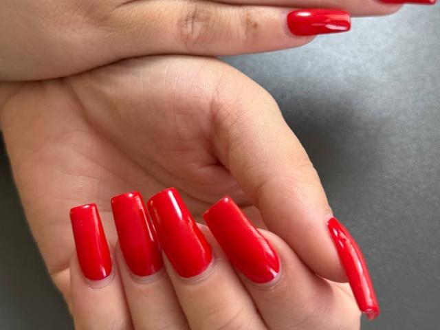 GeraNia's glossy red nails are super long and shiny, stacked neatly on her hand. Her fingers are slightly curled, showing off her perfect manicure.