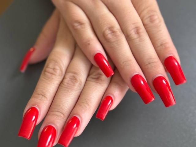 GeraNia's hands with shiny, long red nails, fingers stacked, palm down, showing off her glossy, well-manicured, hot ass nails against a dark background.