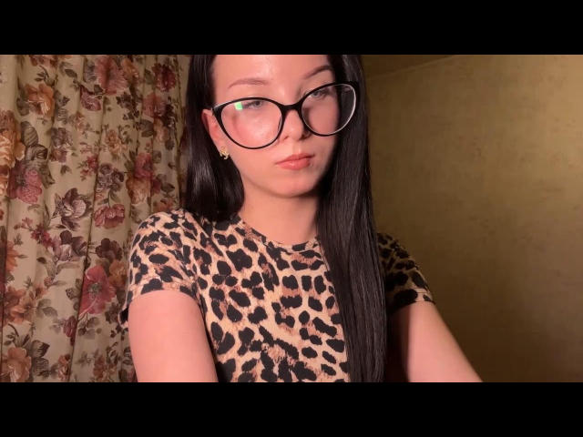 KaterineGrett has long black hair, wears large black-rimmed glasses, and a leopard print shirt. She's got a cute face and a small gold earring. Her ass is not visible.