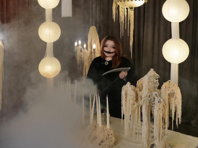 YoureGift, con i capelli rossi, una maglietta nera e un sorriso che mostra un dente nero, tiene un coltello, è in piedi di fronte a decorazioni simili al ghiaccio e lanterne di carta luminose, ed è circondato dalla nebbia..