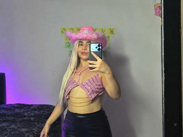 LissyLaurent with long blonde hair, pink fluffy cowboy hat, pink checkered top with chains, black leather skirt, taking a mirror selfie with a smartphone.