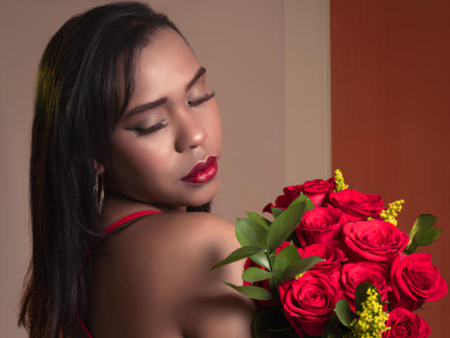 AntonellaVargas with dark hair, red lipstick, and hoop earrings, holding a bouquet of red roses and yellow berries, eyes closed, showing off her tits.