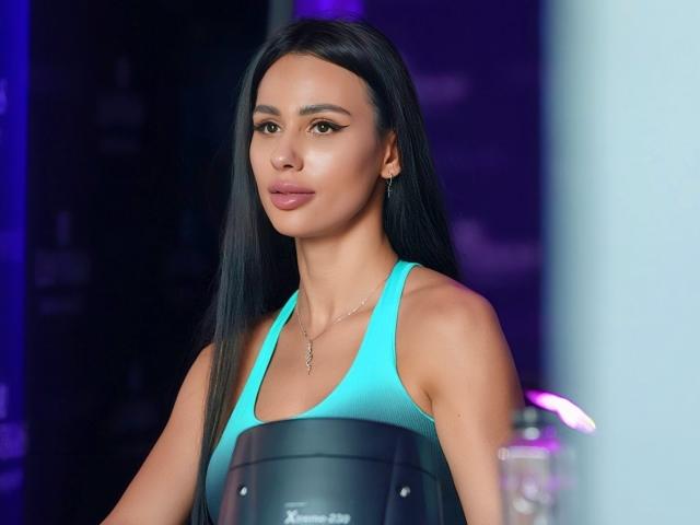 CharlotteAria with long black hair, wearing a turquoise sports bra, holding a black punching bag, has a slim build, small tits, and a subtle smile, in a gym.